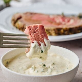 Horseradish sauce in a white bowl with prime rib dipping into it