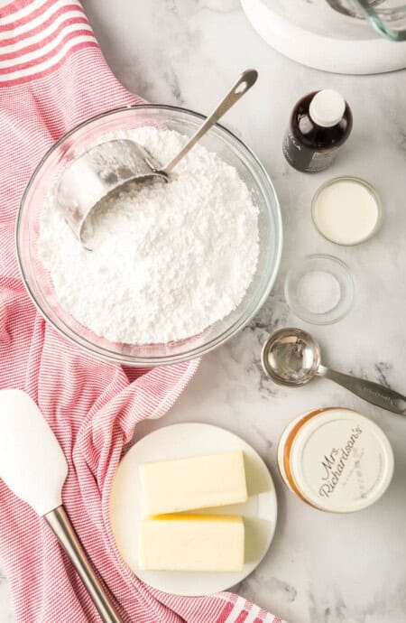 an overhead photo of powdered sugar with a measuring cup, butter, and other ingredients ready to use for baking