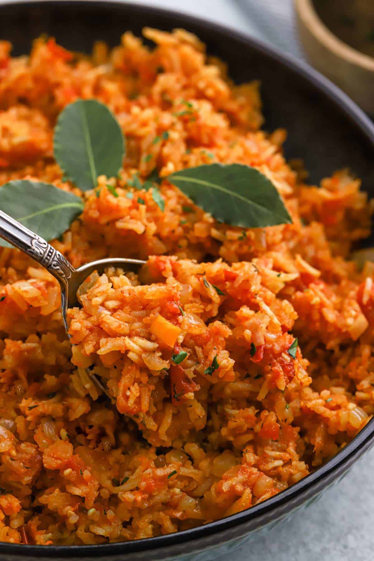 Half of a bowl of jollof rice on the table at an angle with bay leaves on top.