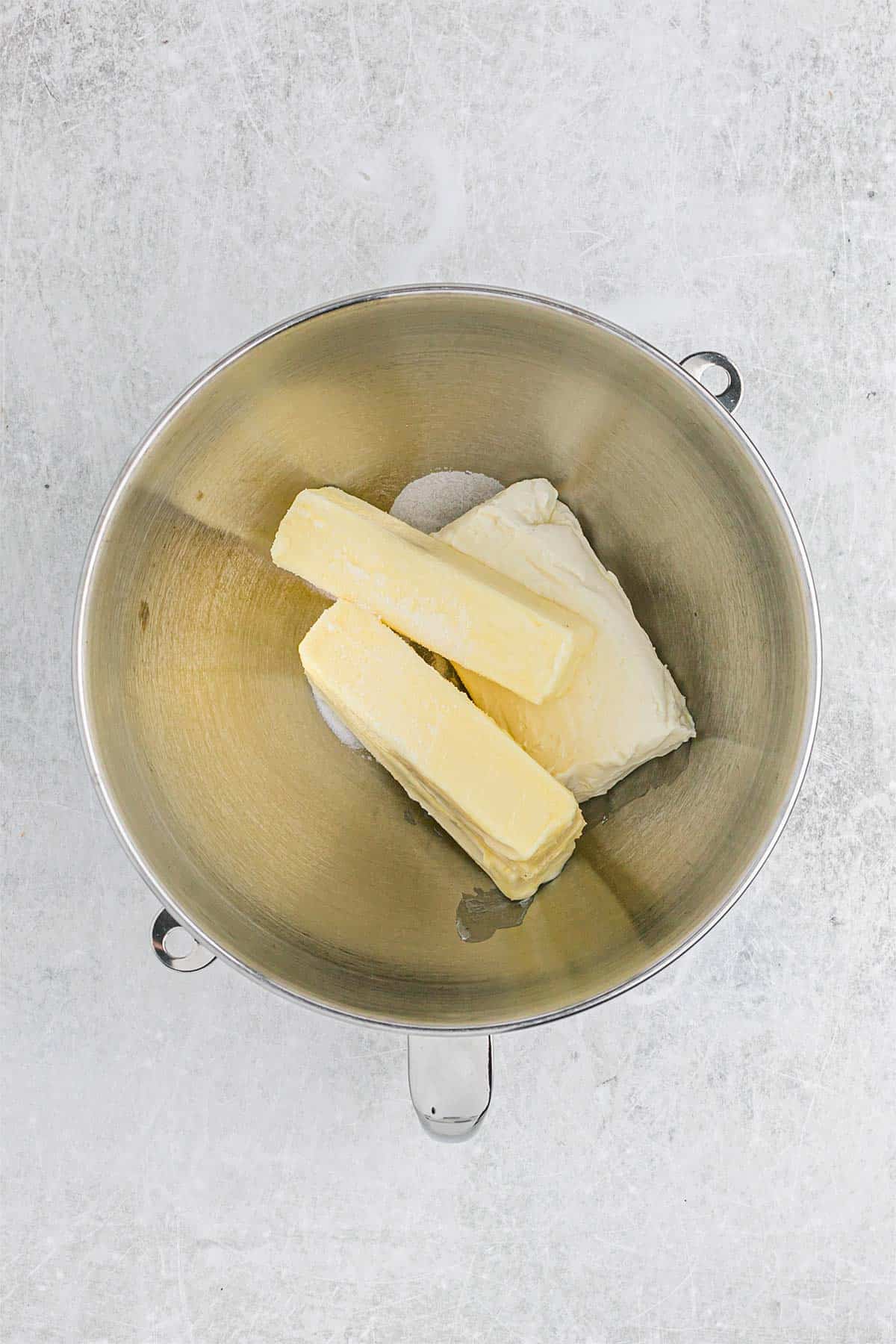 Butter and cream cheese are in the bowl of a stand mixer.