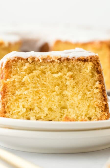 Closeup of a slice of Louisiana Crunch Cake topped with white glaze on a plate with the rest of the cake in the background
