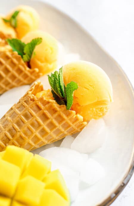 A close up of mango sorbet cones with mint and fresh mango on ice in a tray