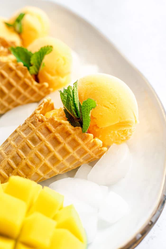 A close up of mango sorbet cones with mint and fresh mango on ice in a tray
