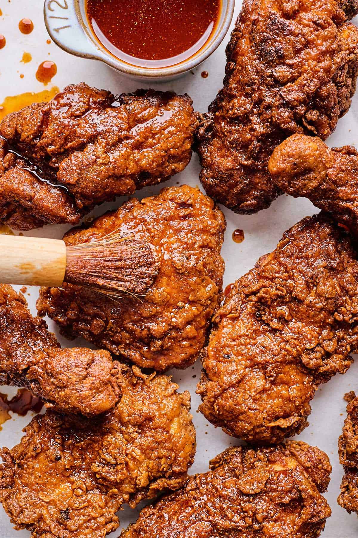 Overhead close up of Nashville Hot Chicken Recipe on a plate with a little pitcher of sauce and a brush adding oil to the chicken.
