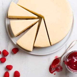New York Cheesecake overhead shot with full cheesecake and four slices with raspberries and raspberry sauce