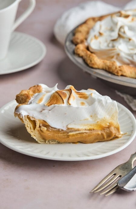 slice of butterscotch pie on a white plate with toasted meringue.