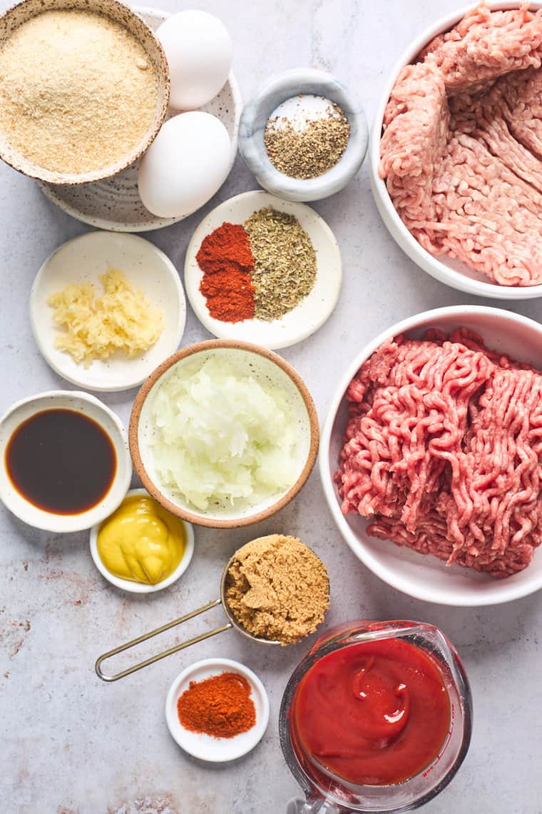 Ground pork, beef, spices, brown sugar, ketchup all in white bowls against a gray background