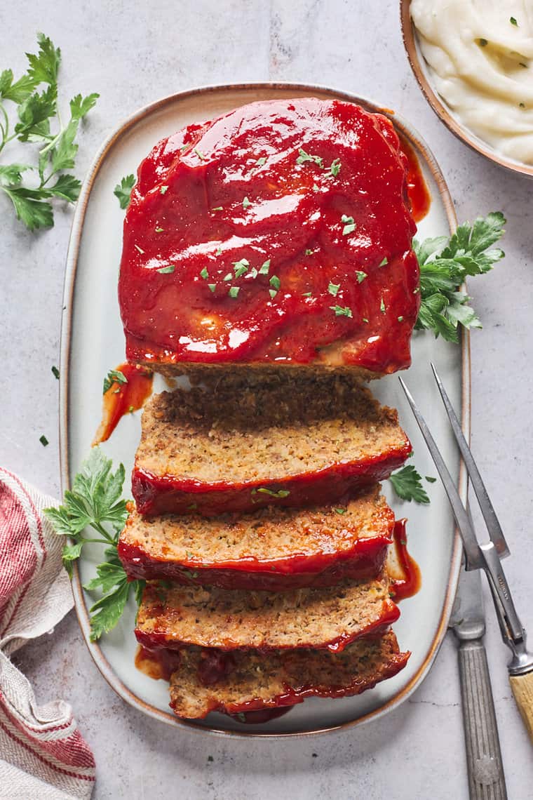 A perfect meatloaf recipe on a white serving platter with slices cut to serve