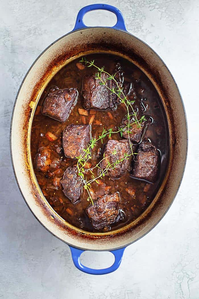 Overhead shot of short ribs braising in liquids in a blue dutch oven out of the oven