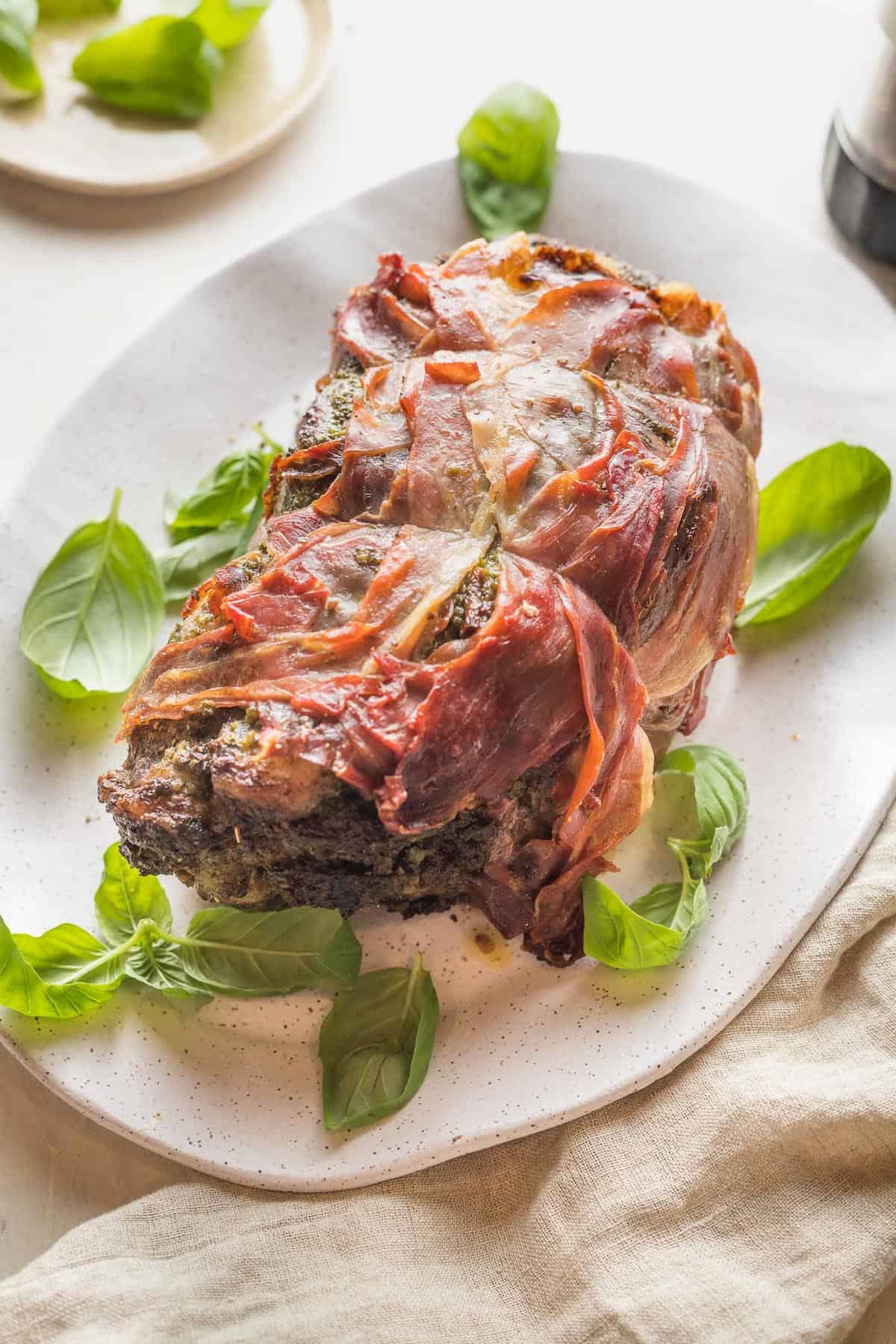 A white serving platter with a prosciutto wrapped beef roast.