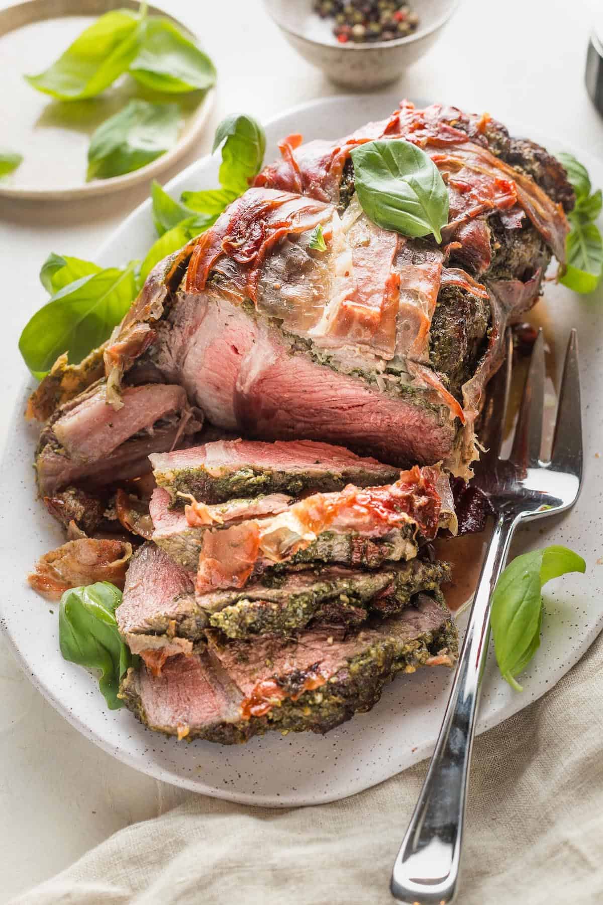 A white serving platter with a prosciutto wrapped beef roast.
