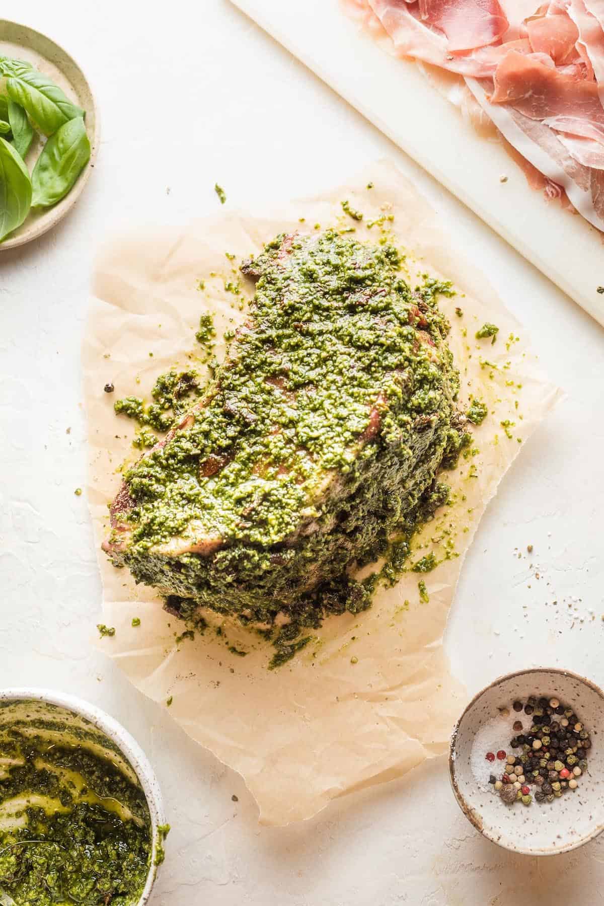 Pesto rubbed all over a beef roast on a cutting board.