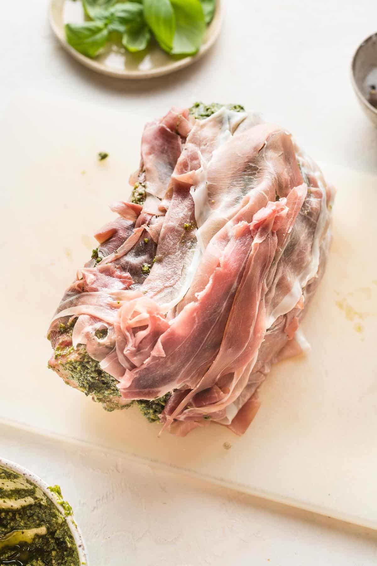 A prosciutto wrapped beef roast on a cutting board.