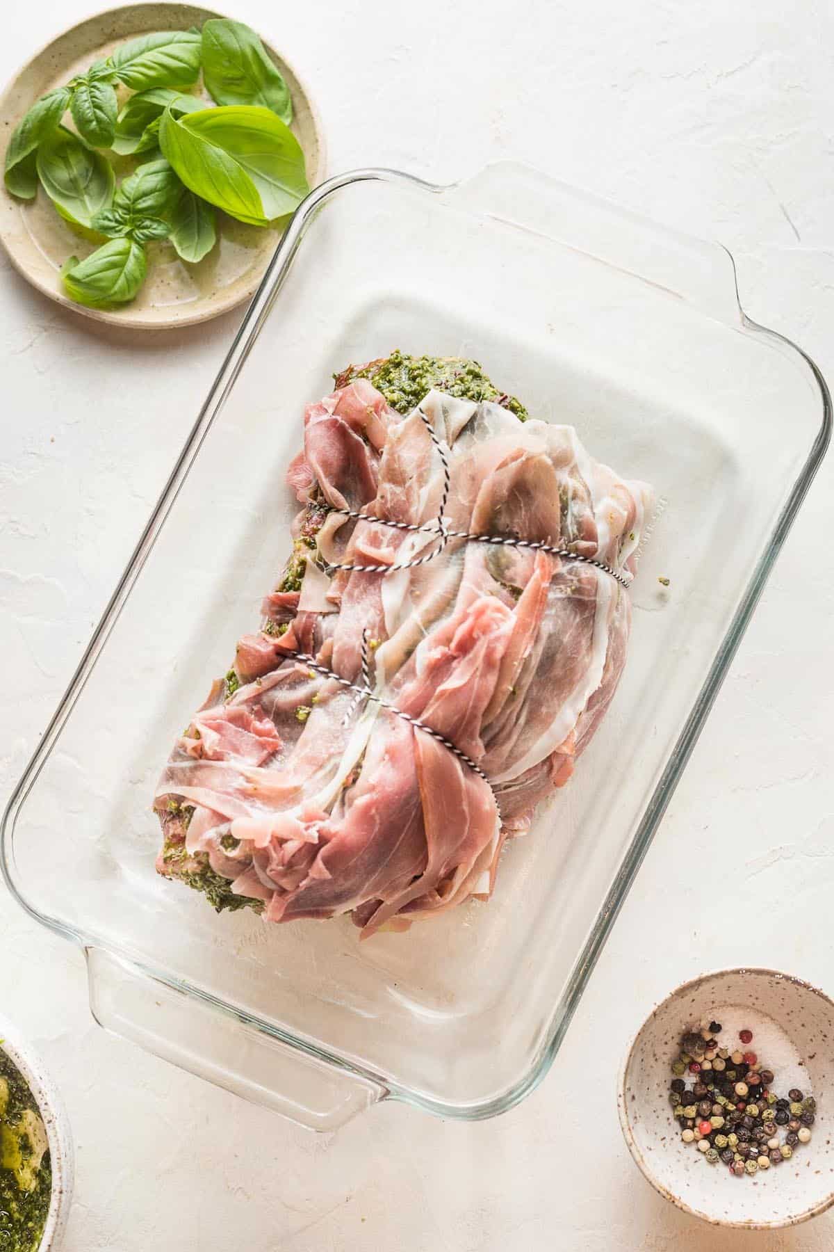 A prosciutto wrapped beef roast in a glass baking dish.