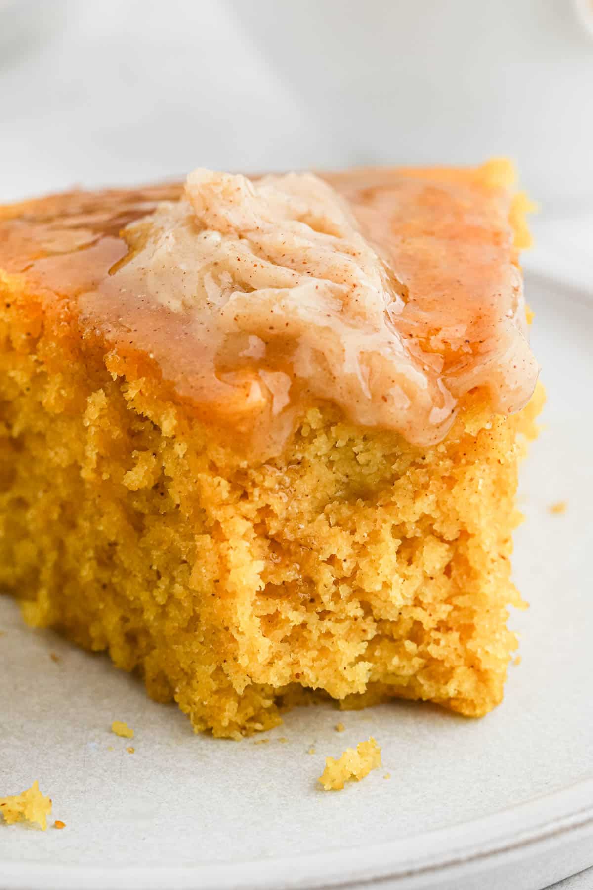 A slice of cornbread with pumpkin on a plate with cinnamon butter melting on top and a bite missing from the front.