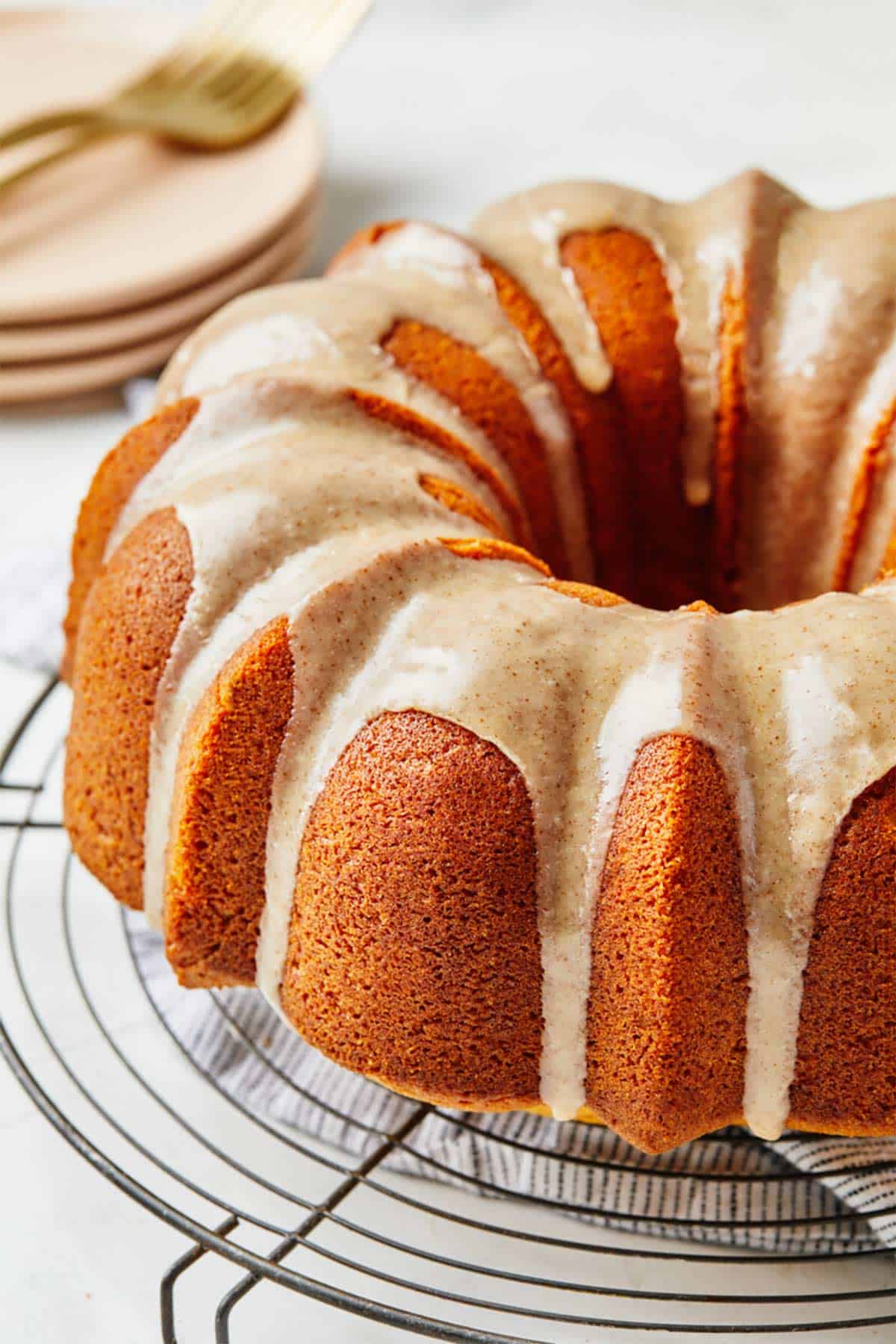 A pumpkin bundt cake recipe on a wire rack on the table with a stack of plates in the background.