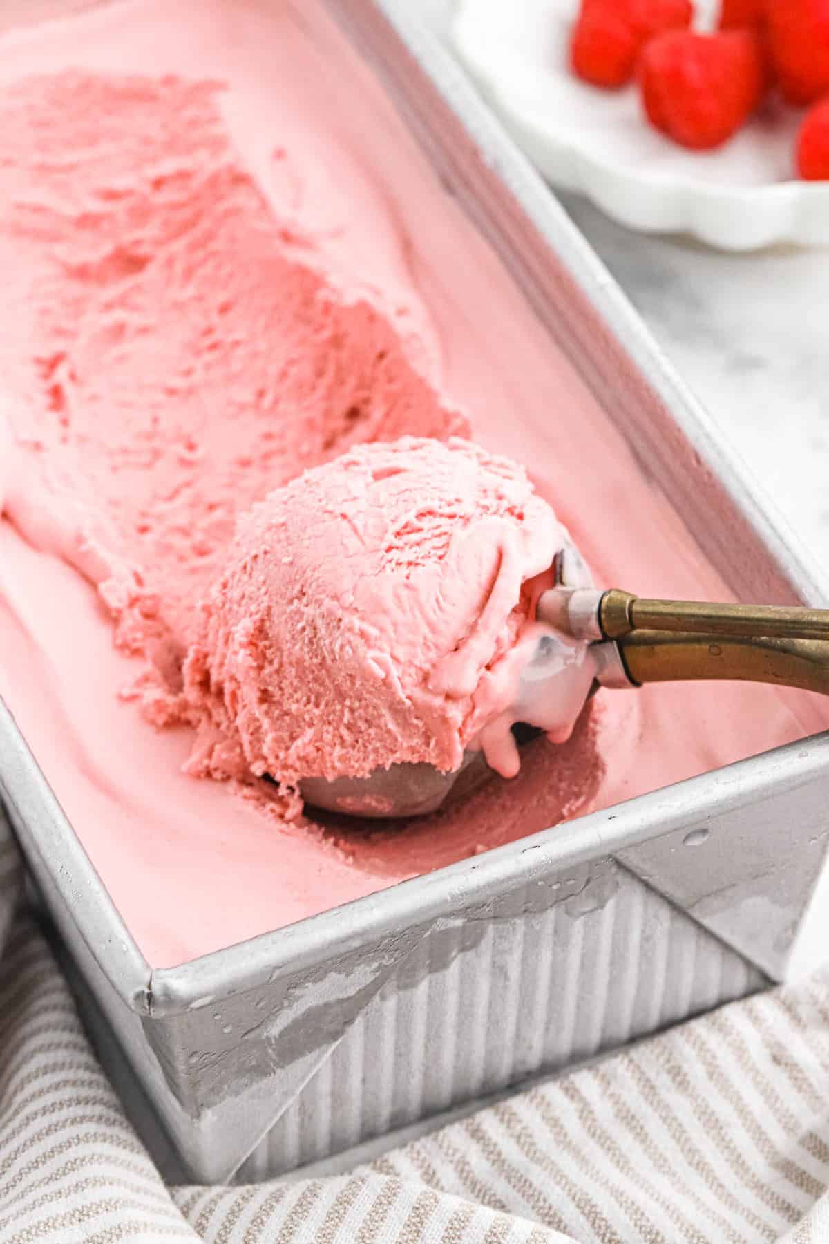 raspberry ice cream Large tray of raspberry ice cream with an ice cream scooper filled with a scoop of ice cream in it.
