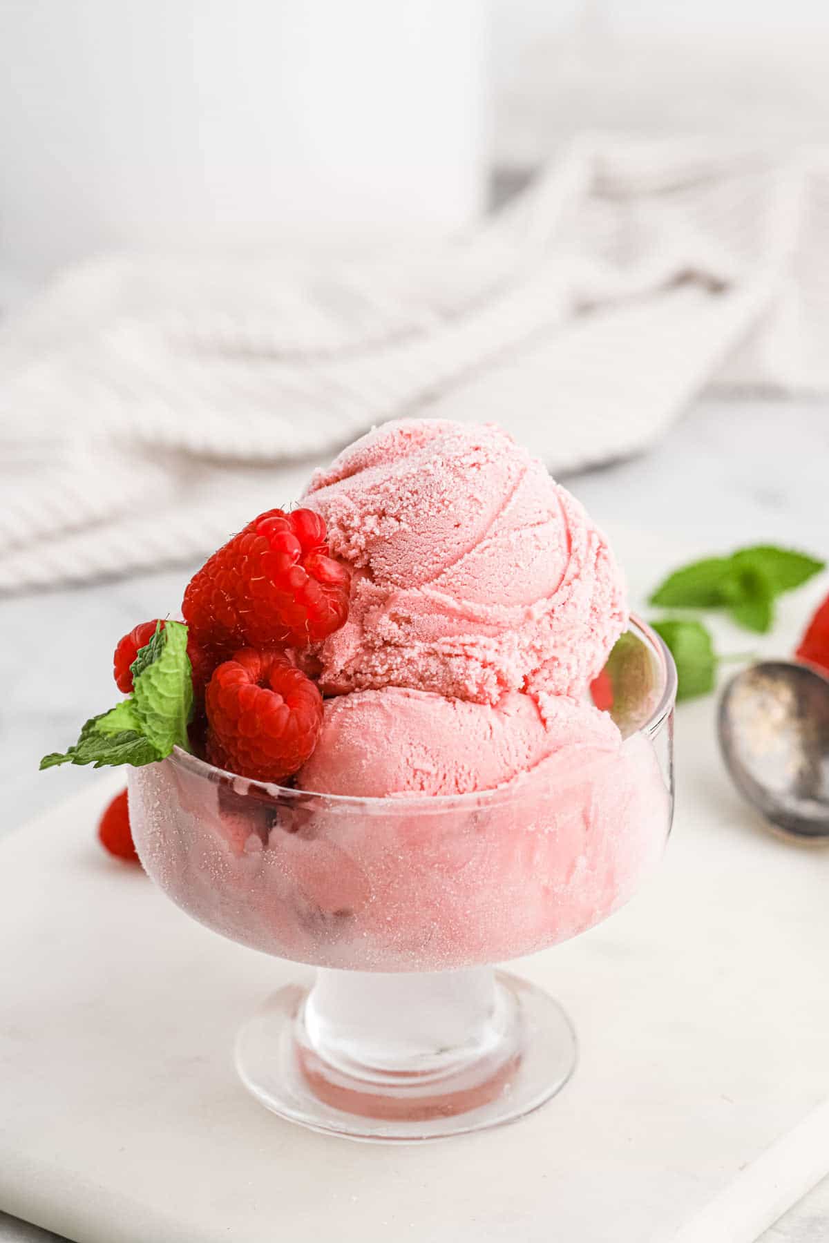 raspberry ice cream Raspberry ice cream scooped into a glass dessert cup and topped with fresh raspberries.
