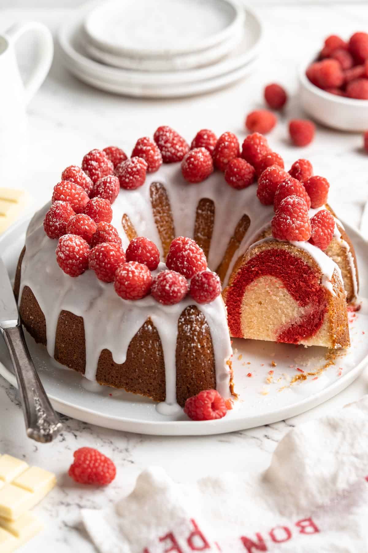 White chocolate raspberry bundt cake with slice missing on a white plate
