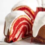 A spatula pulling out a slice of red velvet marble cake from the whole cake.