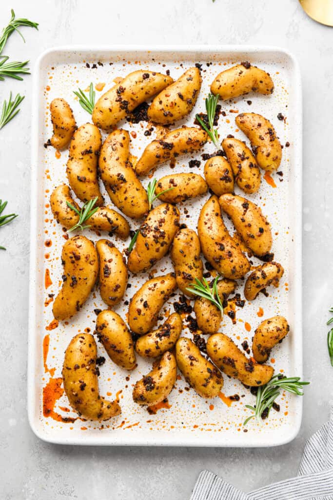 Roasted fingerling potatoes on a white baking sheet on white countertop.