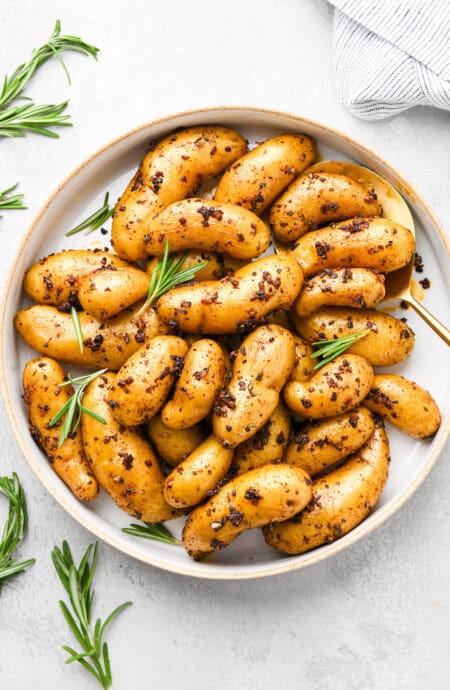 Roasted fingerling potatoes topped with herbs on a white plate ready to serve on white background