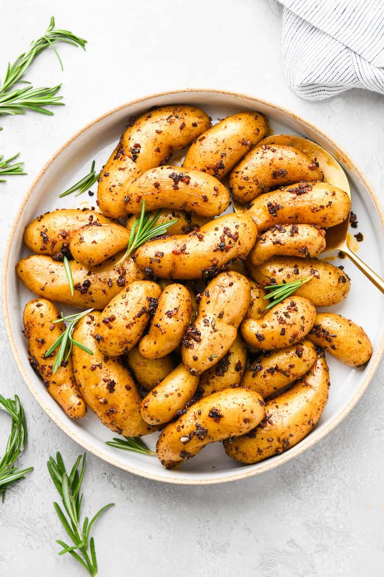 Roasted fingerling potatoes topped with herbs on a white plate ready to serve on white background