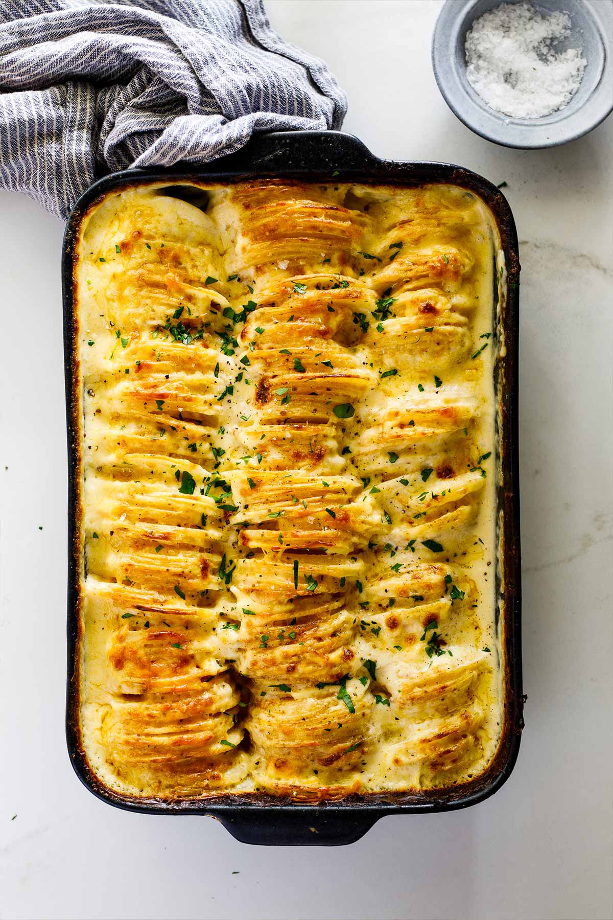 Cheesy potatoes served up on a plate with casserole dish in background.