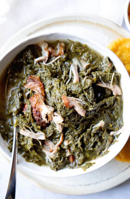 A close up of a white bowl filled with southern mustard greens recipe with smoked turkey with hot water cornbread