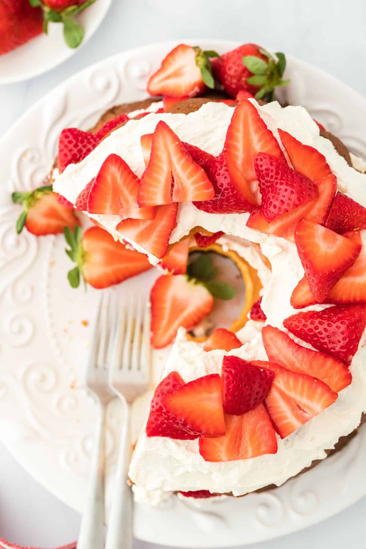 Overheat shot of strawberry shortcake pound cake with a slice missing, placed on a white plate next to two forks