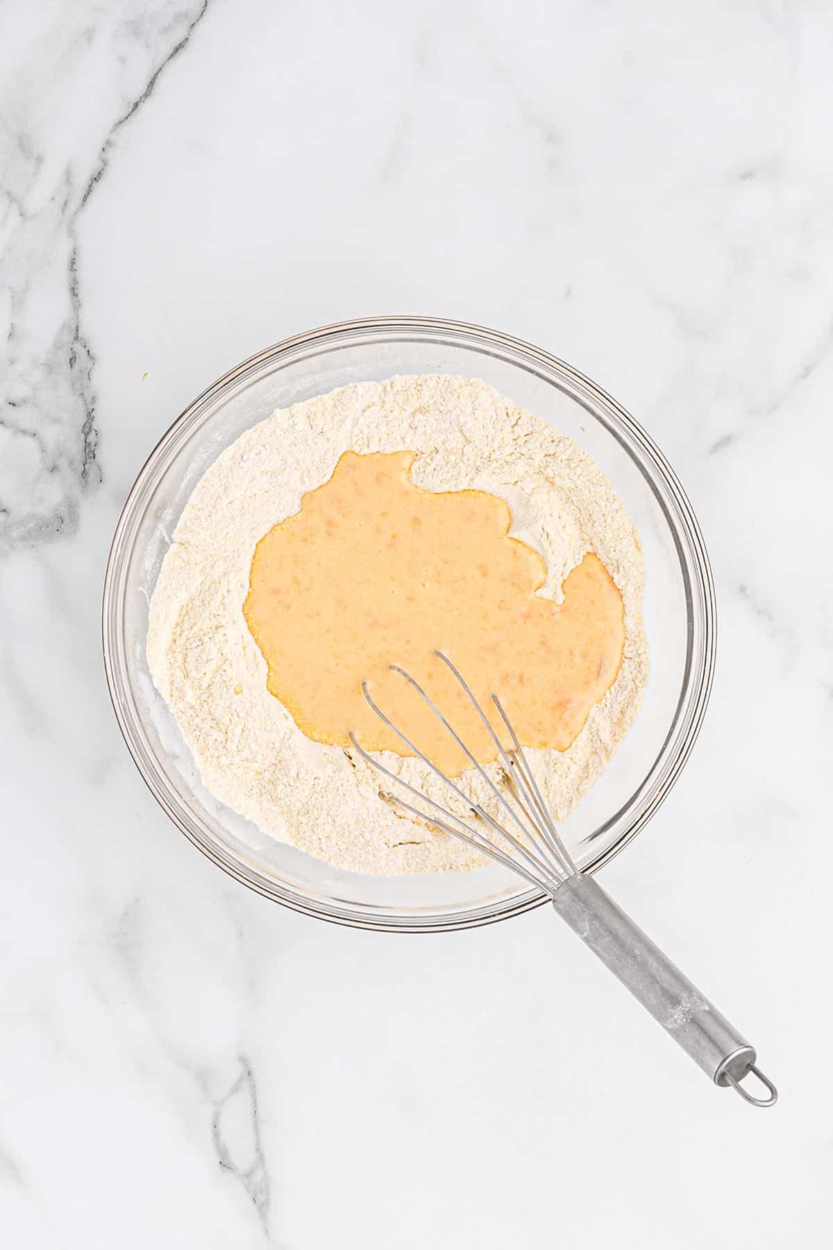 Blended wet ingredients added to the flour mixture in a glass bowl.