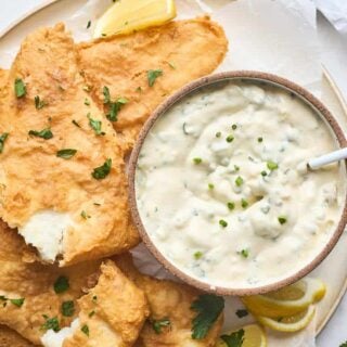 Pieces of fried fish on a white platter with a bowl of the best tartar sauce recipe with a small spoon