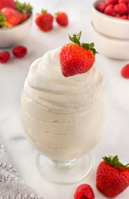 A glass of whipped cream with a strawberry on top and others in the background