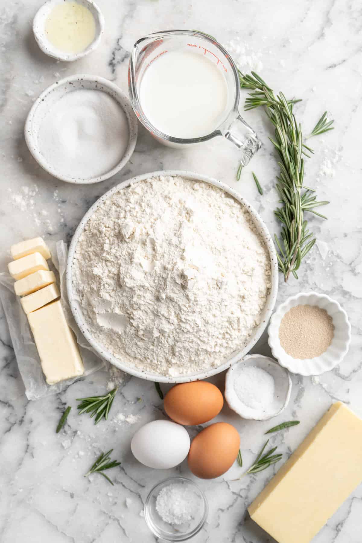 Ingredients to make fresh dinner rolls in bowls on a white surface.